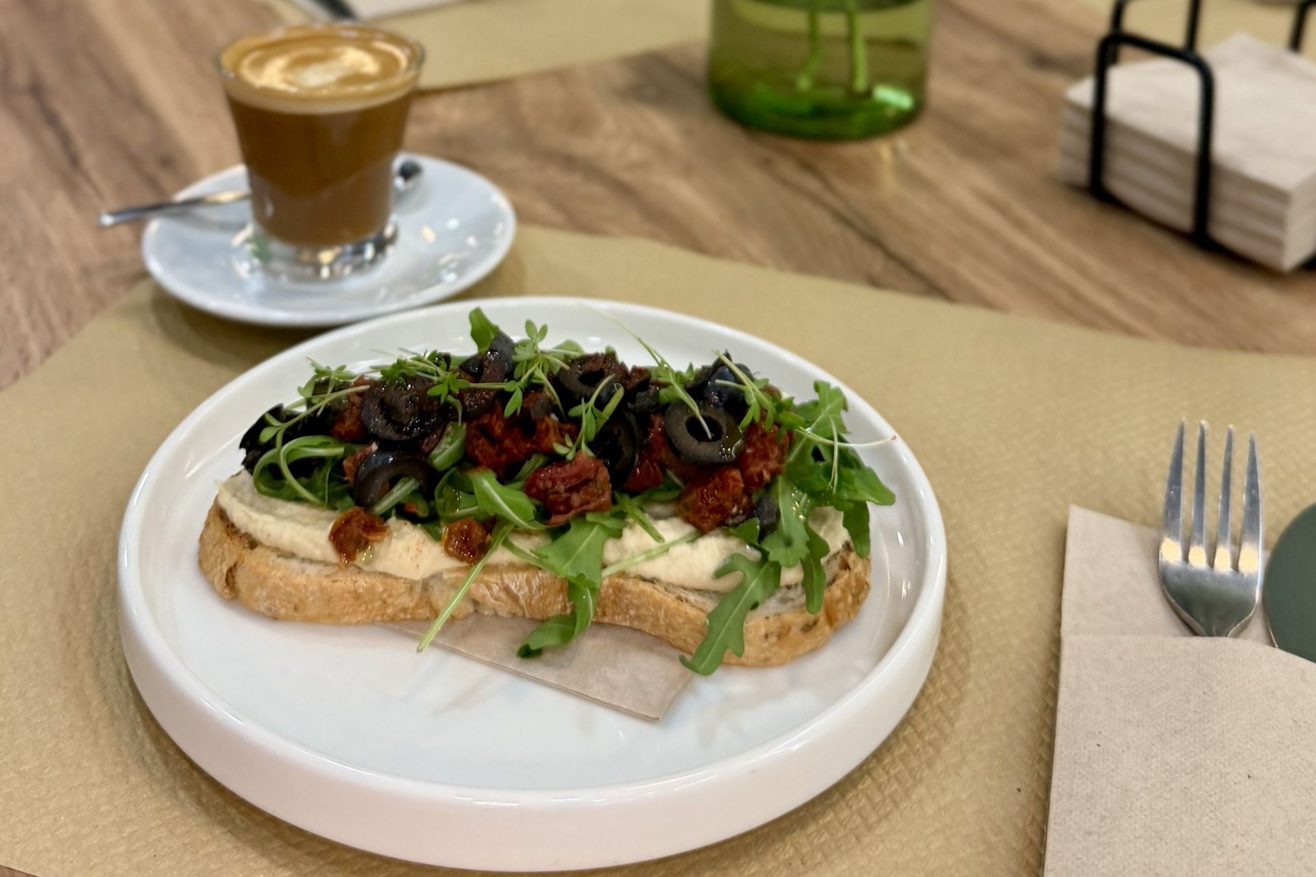 Tostada de hummus con tomate seco, aceitunas negras y rúcula, desayuno sin gluten en Gato Blanco Valencia