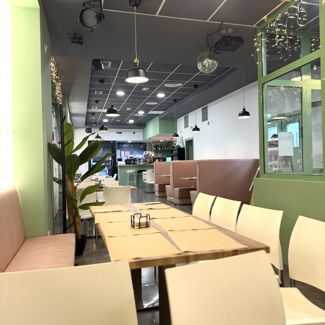 Dining room of the celiac-friendly restaurant Gato Blanco, with long wooden tables, pink benches and green walls