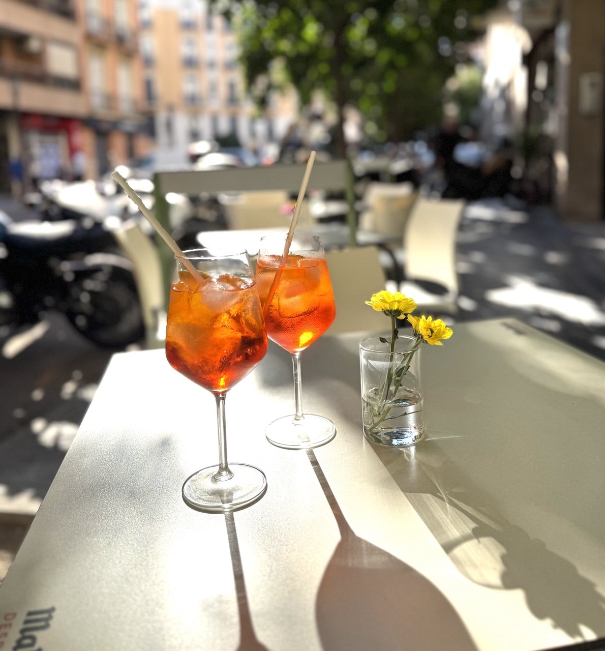 Dos copas de spritz naranja con hielo y una flor amarilla sobre una mesa de la terraza de Gato Blanco
