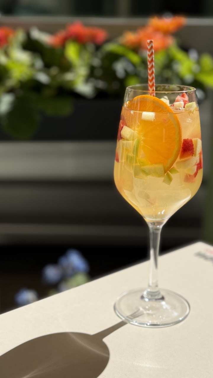 Copa con bebida fresca de naranja y fruta troceada con pajita de rayas, en la terraza de Gato Blanco