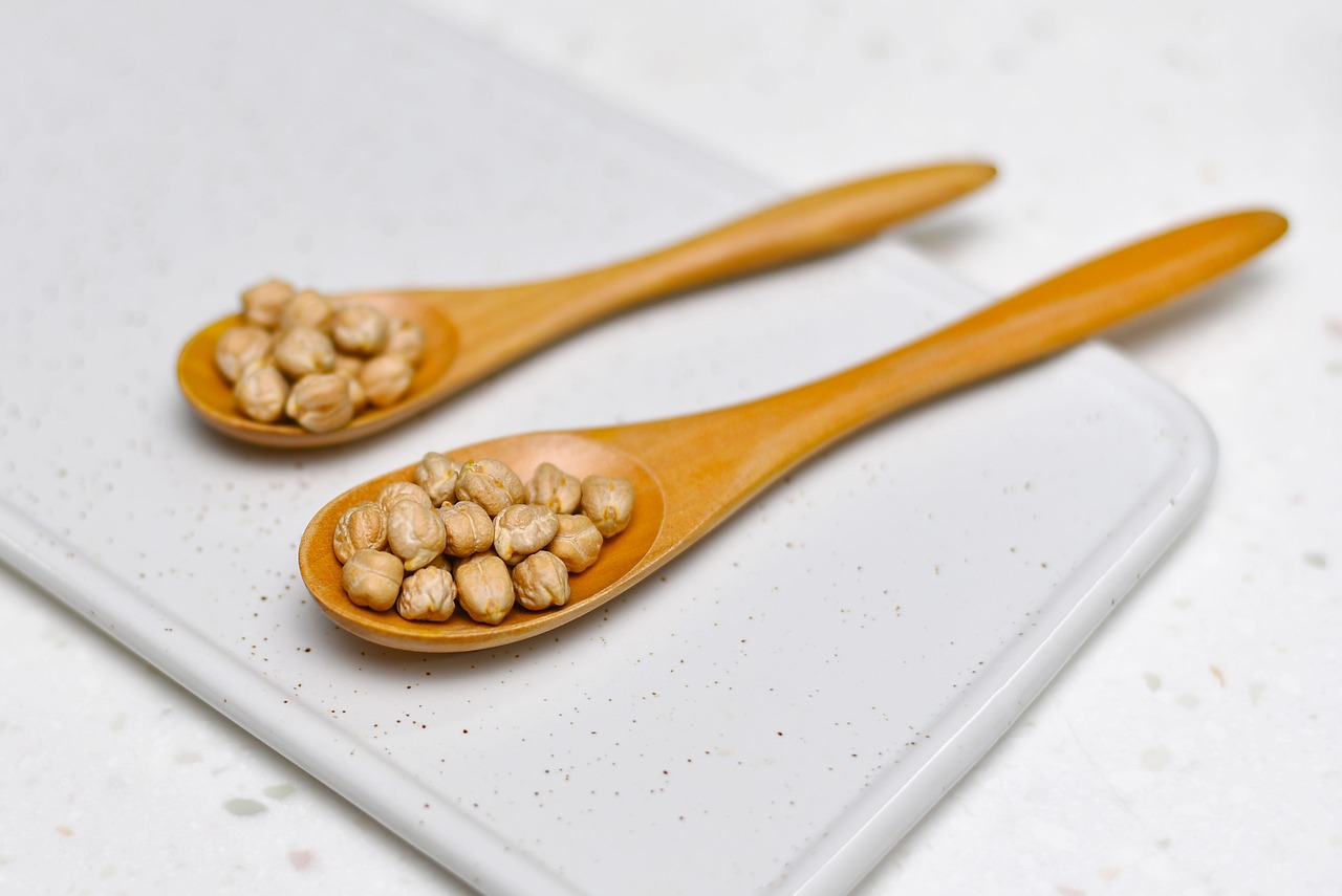 Two wooden spoons with dried chickpeas on a white board, legumes that are safe for celiacs