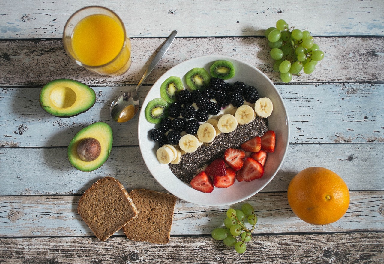 Mesa de desayuno con un bol de fruta fresca, aguacate y pan, ejemplos de alimentos sin gluten y sin lactosa