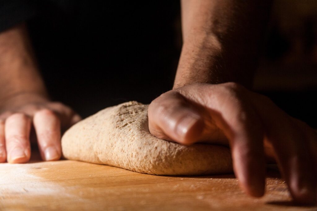 Manos amasando una masa de pan sobre una tabla de madera, el gluten da elasticidad a la masa