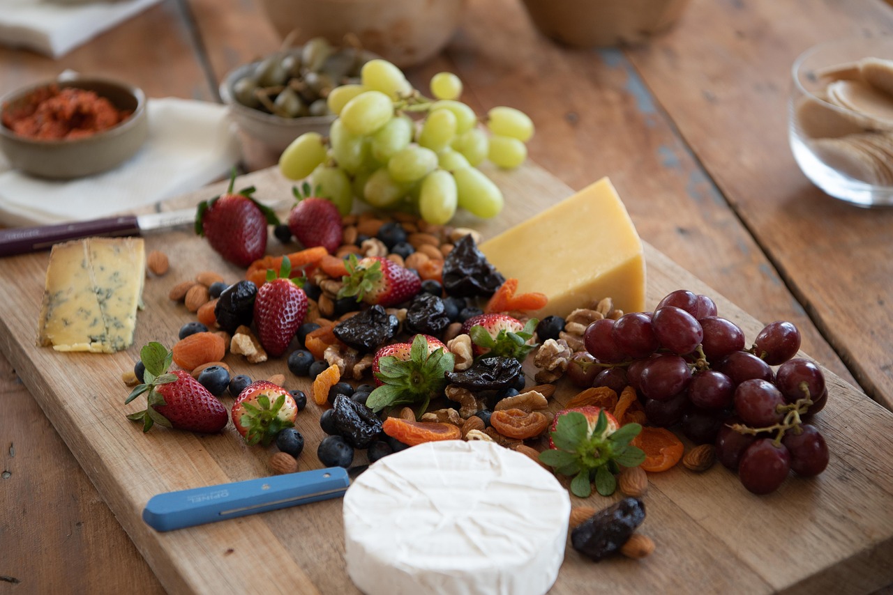 Tabla de madera con queso azul, cheddar y brie, fresas, uvas, arándanos y frutos secos, alimentos sin gluten por naturaleza
